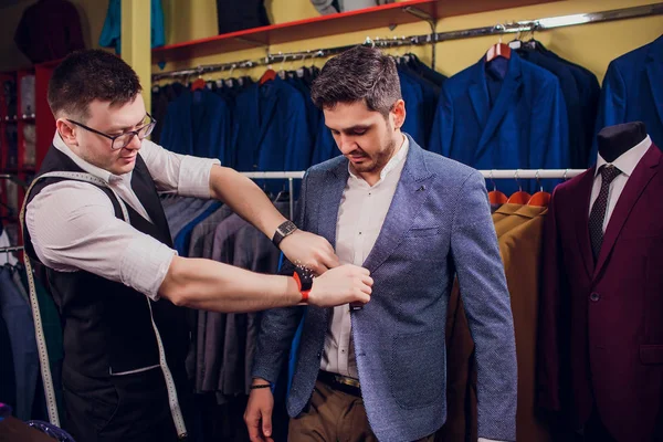 Satır karşı klasik yelek işadamı dükkanda uygun. Adam başka bir takım elbise giyim mağazası denemede yardımcı olur.