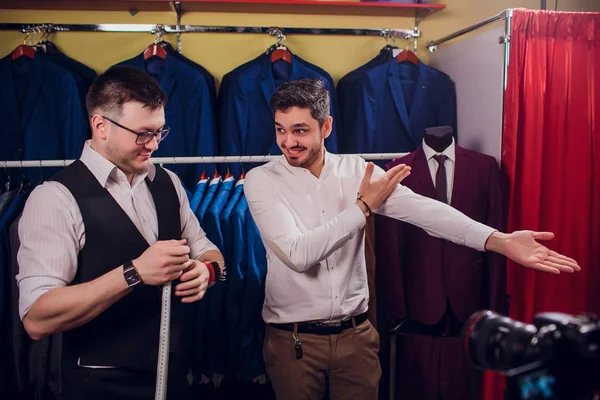 Empresário em colete clássico contra ternos de linha na loja. Homem ajuda outra tentativa em terno na loja de roupas — Fotografia de Stock