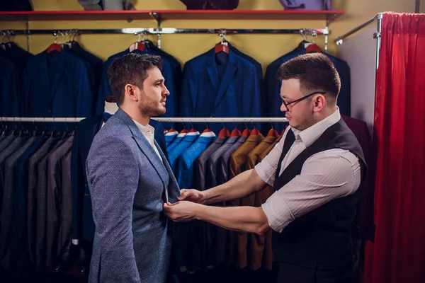 Satır karşı klasik yelek işadamı dükkanda uygun. Adam başka bir takım elbise giyim mağazası denemede yardımcı olur.