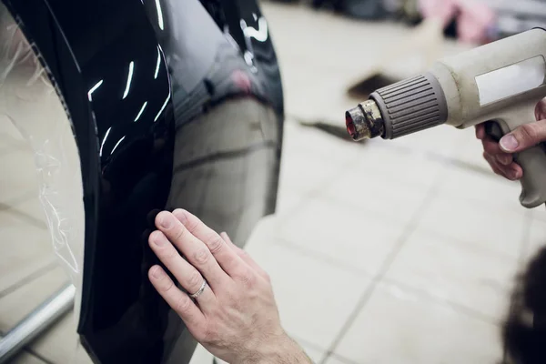 Worker hands installs car paint protection film wrap bumper