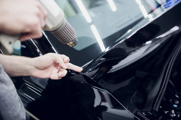 Worker hands installs car paint protection film wrap hood