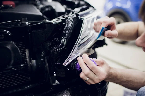 Worker hands installs car paint protection film wrap headlamp