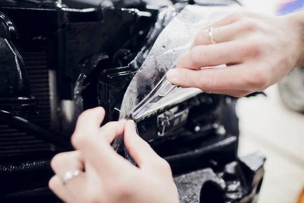 Worker hands installs car paint protection film wrap auto headlight