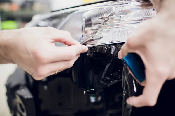 Robotnik ręce instaluje samochód farby ochrony film wrap auto reflektorów — Zdjęcie stockowe