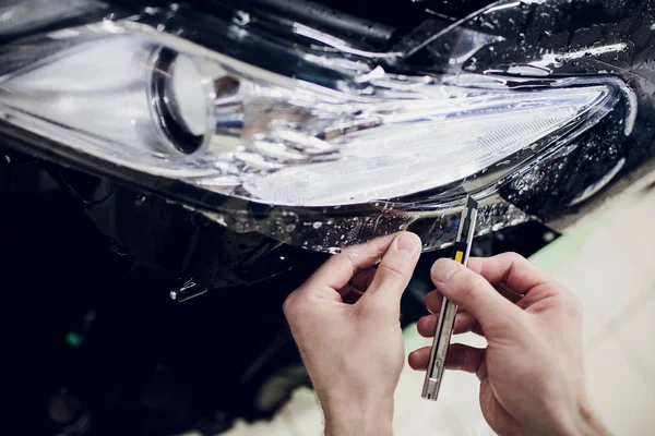 Worker hands installs car paint protection film wrap auto headlight