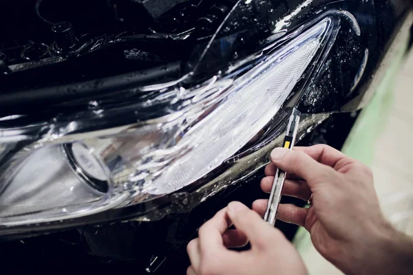 Worker hands installs car paint protection film wrap auto headlight