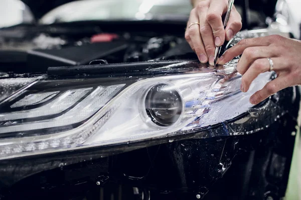 Worker hands installs car paint protection film wrap auto headlight