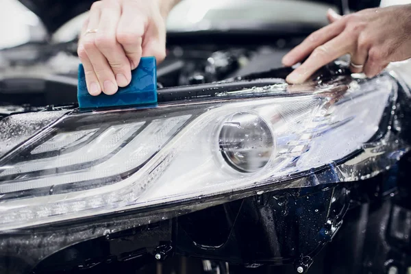 Worker hands installs car paint protection film wrap auto headlight