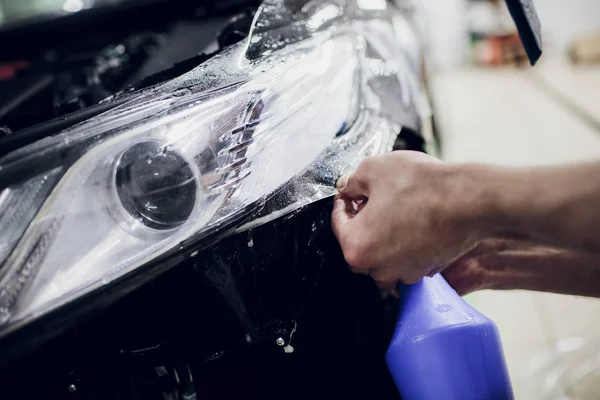 Worker hands installs car paint protection film wrap auto headlight