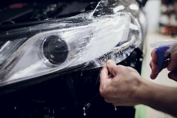 Mãos do trabalhador instala carro pintura proteção filme envoltório auto farol — Fotografia de Stock