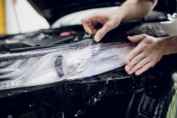 Manos de trabajador instala protección de pintura del coche película envoltura auto faro — Foto de Stock