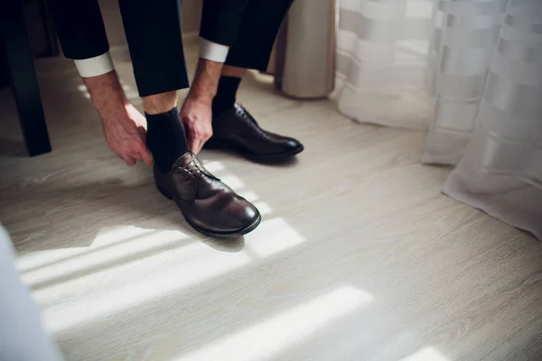 Grooms morning. Wedding accessories. Shoes. The groom ties hoelaces on his shoes