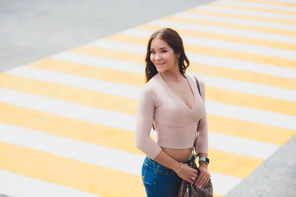 Felice giovane studentessa attraversando strada e cappello ribaltamento contro sfondo urbano della città . — Foto Stock