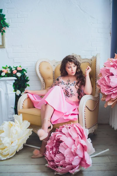 Attraente giovane donna in abito elegante seduta in studio interno decorato con fiori. Bella ragazza sorridente fresca in posa con i fiori — Foto Stock