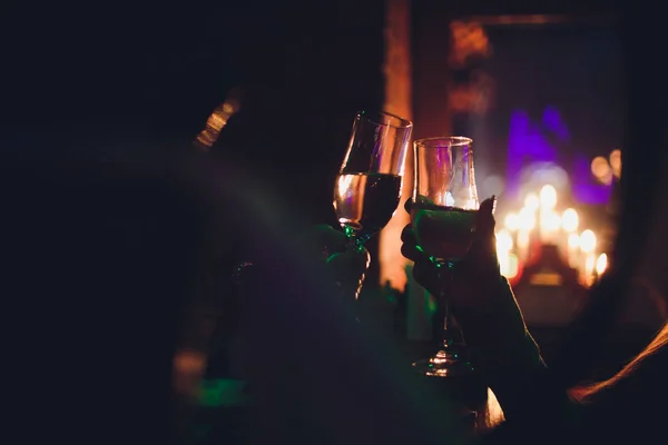 Iluminaciones navideñas y copas de champán. Manos de personas con copas de champán, celebrando y brindando en honor a la Navidad y Feliz Año Nuevo. Pareja animando con flautas de champán . —  Fotos de Stock