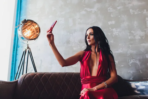 黒い髪と夜メイク、身に着けている豪華な赤いドレスでゴージャスな女性のファッション スタジオ写真。ターコイズ ブルーのネオン ライト映画スポット ライト、selfie になります — ストック写真