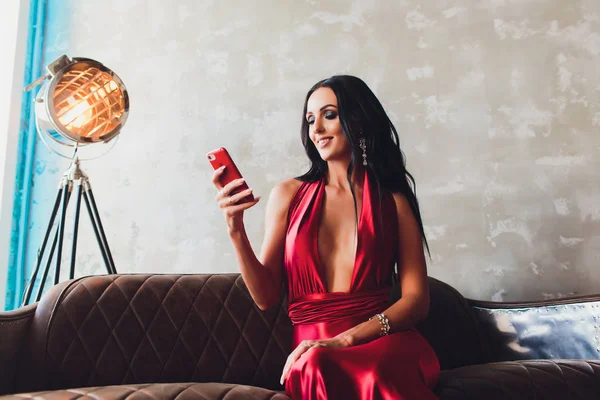 Modestudio Foto von wunderschönen Frau mit dunklen Haaren und abends Make-up, trägt luxuriöse rote Kleid. Neontürkisfarbener Scheinwerfer macht ein Selfie — Stockfoto