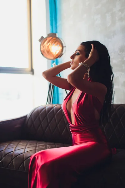 Foto de estudio de moda de mujer hermosa con cabello oscuro y maquillaje de noche, lleva vestido rojo de lujo. luces turquesa neón proyector de película — Foto de Stock