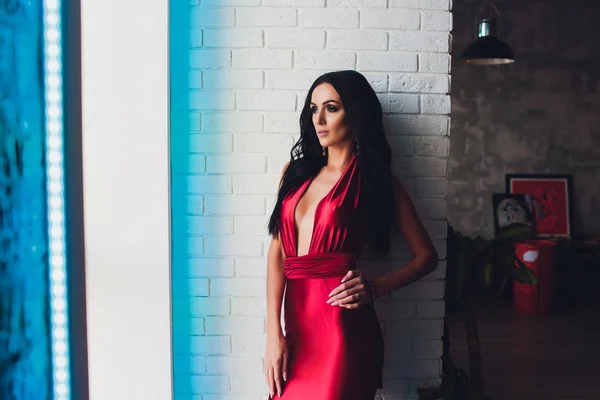 Μόδα στούντιο φωτογραφία πανέμορφη γυναίκα με σκούρα μαλλιά και βραδινό μακιγιάζ, πολυτελές κόκκινο φόρεμα φοράει. φώτα νέον τυρκουάζ — Φωτογραφία Αρχείου