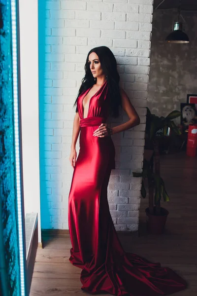 Модна студійна фотографія чудової жінки з темним волоссям і вечірнім макіяжем, носить розкішну червону сукню. неонове бірюзове світло — стокове фото