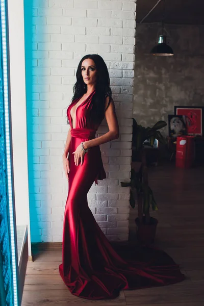 Модна студійна фотографія чудової жінки з темним волоссям і вечірнім макіяжем, носить розкішну червону сукню. неонове бірюзове світло — стокове фото