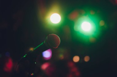 Mikrofon bir stand için hazır canlı müzik performansı veya karaoke gecesi yumuşak bokeh ışıkları ve insan siluetleri ile arka planda. Kavramı için müzik şarkı olay, iyi vakit geçiriyor.