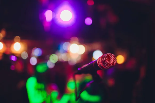 Microphone sur un stand prêt pour la performance musicale en direct ou soirée karaoké avec des lumières bokeh douces et des silhouettes de personnes en arrière-plan. Concept pour l'événement de chant musical, passer un bon moment . — Photo