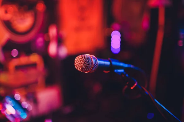 Microfoon op een staan klaar voor live muziek prestaties of karaoke avond met zachte bokeh verlichting en mensen silhouetten in de achtergrond. Concept voor muzikale zang evenement, met een goede tijd. — Stockfoto