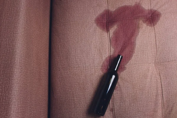 Rött vin spillda på en brun soffa soffa. mörk flaska rött vin tappade — Stockfoto