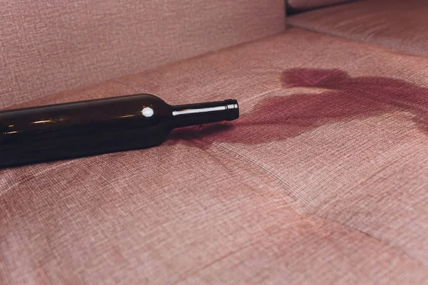 Rött vin spillda på en brun soffa soffa. mörk flaska rött vin tappade — Stockfoto