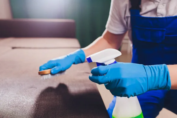 Cropped image. Cleaning concept. Male hand in light blue protective gloves cleaning sofa couch in the room. — Stock Photo, Image