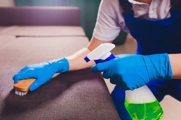 Imagem cortada. Conceito de limpeza. Mão masculina em azul claro luvas de proteção de limpeza sofá sofá no quarto . — Fotografia de Stock