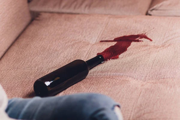 Red wine spilled on a brown couch sofa. dark bottle of red wine dropped