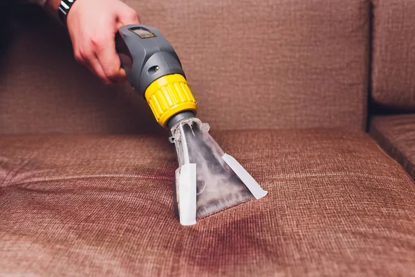Sofa chemical cleaning with professionally extraction method. Upholstered furniture. Early spring cleaning or regular clean up. Dry cleaners in light protective glove employee removing dirt from