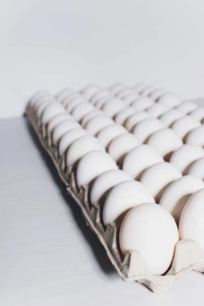 Ovos brancos de uma galinha em embalagem inofensiva, de papelão em um fundo branco. — Fotografia de Stock