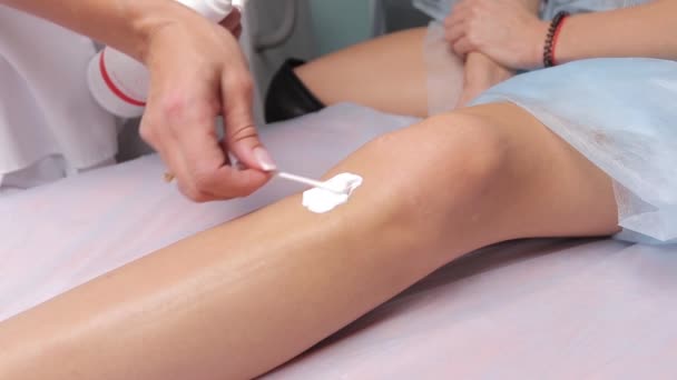 Beautician applying a cream exfoliating on the legs of a young woman. — Stock Video