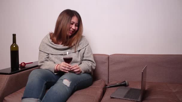 Mujer en casa sentada en el sofá con un ordenador portátil y vino. mujer ríe viendo una película . — Vídeo de stock