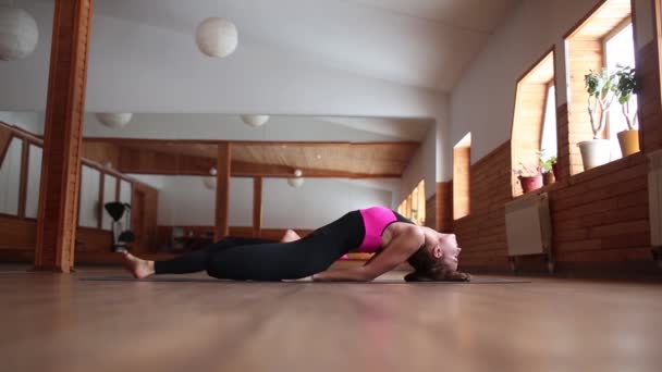 Jovem mulher yogi atraente praticando conceito de ioga, alongamento no exercício Matsyasana, Peixe pose, exercitando-se, vestindo sportswear, comprimento total, fundo estúdio loft branco. Vista lateral . — Vídeo de Stock