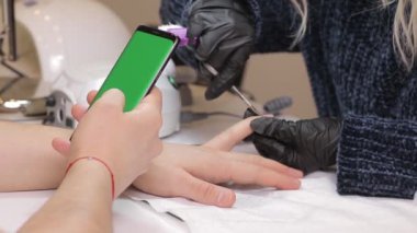 Yeşil ekran smartphone. sosyal medya modern güzel dokunmatik telefon kullanarak kaydırma adam. Güzellik salonunda manikür. O onun koluna kuruması tırnak cilası bekler.