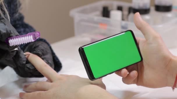 Πράσινη οθόνη smartphone. ο άνθρωπος κύλιση μέσων κοινωνικής δικτύωσης χρησιμοποιώντας μοντέρνα ωραία οθόνη αφής τηλέφωνο. Μανικιούρ στο σαλόνι ομορφιάς. Περιμένει για το βερνίκι νυχιών να στεγνώσει στο χέρι. — Αρχείο Βίντεο