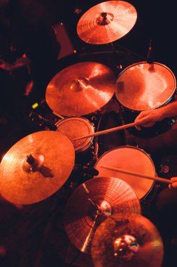 Adam siyah arka plana yakın sopalarla müzik aleti çalıyor. Davul çalan bir müzik konsepti, sahnede güzel bir ışıklandırma..