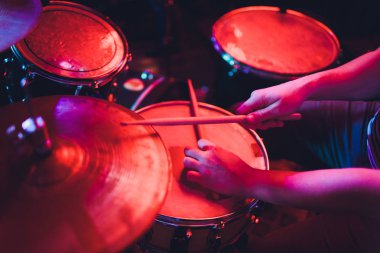 Adam siyah arka plana yakın sopalarla müzik aleti çalıyor. Davul çalan bir müzik konsepti, sahnede güzel bir ışıklandırma..