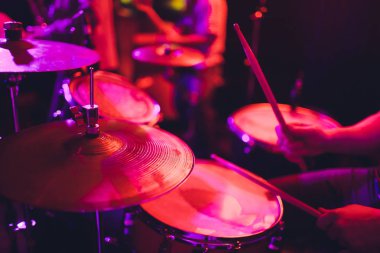 Adam siyah arka plana yakın sopalarla müzik aleti çalıyor. Davul çalan bir müzik konsepti, sahnede güzel bir ışıklandırma..
