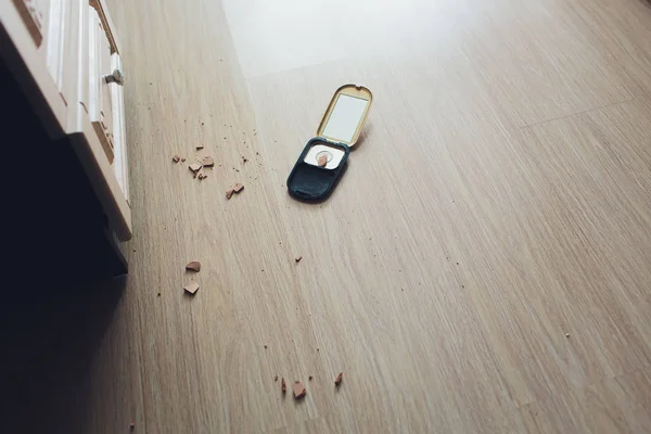 A black compact powder case that fall on the floor till the powder inside is broken. By its powder is spread on the white table. Cosmetic and beauty concept.