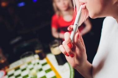Elektronik Sigara, teknoloji sigara. Tütün sistemi Iqos. Restoran bulanık arka planda kadın el.