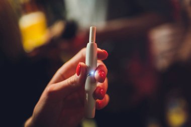 Elektronik Sigara, teknoloji sigara. Tütün sistemi Iqos. Restoran bulanık arka planda kadın el.