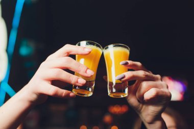 Kokteyl ile tost arkadaşlar closeup çekim. Genç insanlar aperatifinde içiyor. Arkadaşlar el kızartma suyu cam üzerinde odaklanarak alan sığ derinliği. Bir kokteyl camı tutan ellerin yakın.