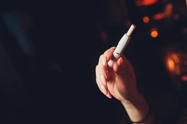 Ηλεκτρονικά τσιγάρα, τεχνολογία τσιγάρων. Το σύστημα καπνού, ο Ικίος. Θηλυκό χέρι σε θολό φόντο του εστιατορίου. μαύρη θήκη. — Φωτογραφία Αρχείου