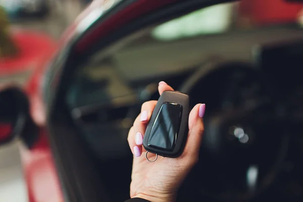 Mano de una chica con una llave de coche en la mano, sobre un fondo rojo del coche . — Foto de Stock