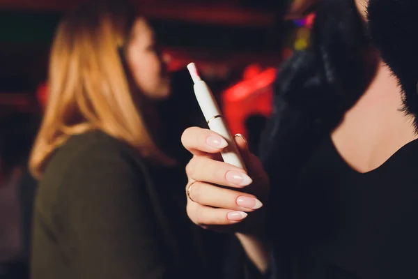 Sigarette elettroniche, sigarette tecnologiche. Sistema tabacco IQOS. mano femminile su sfondo sfocato del ristorante . — Foto Stock